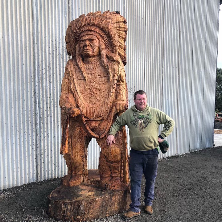 Paul Stafford standing beside a large carved Native American chief sculpture