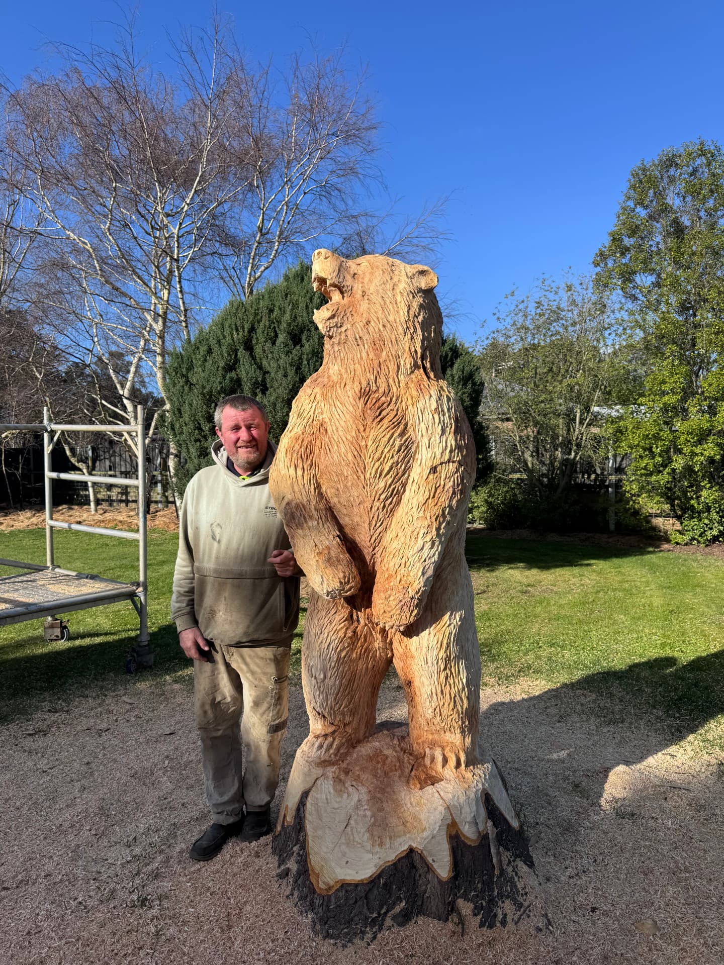 Paul Stafford standing beside a large hand-carved timber bear sculpture